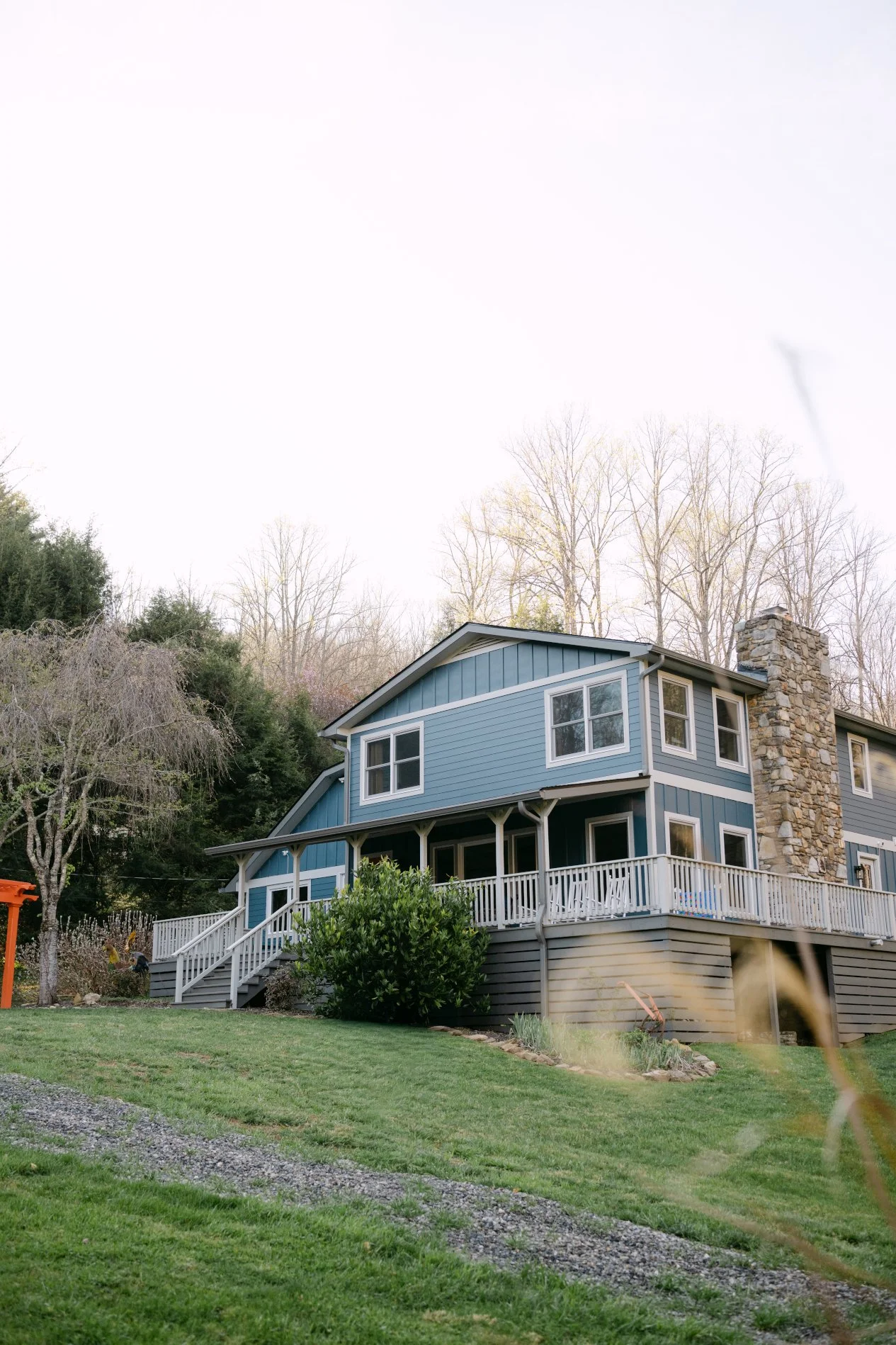 The blue Main House at Caya Azul, a private mountain retreat near Asheville, overlooking the pond and surrounded by the wooded Blue Ridge landscape.