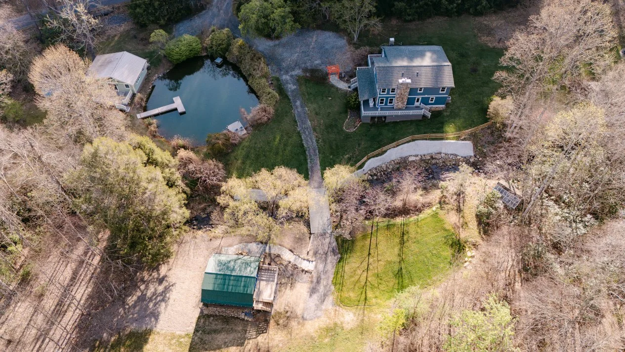 Aerial view of Caya Azul, a private mountain retreat near Asheville, showing the Main House, pond, surrounding forest, and Blue Ridge landscape.