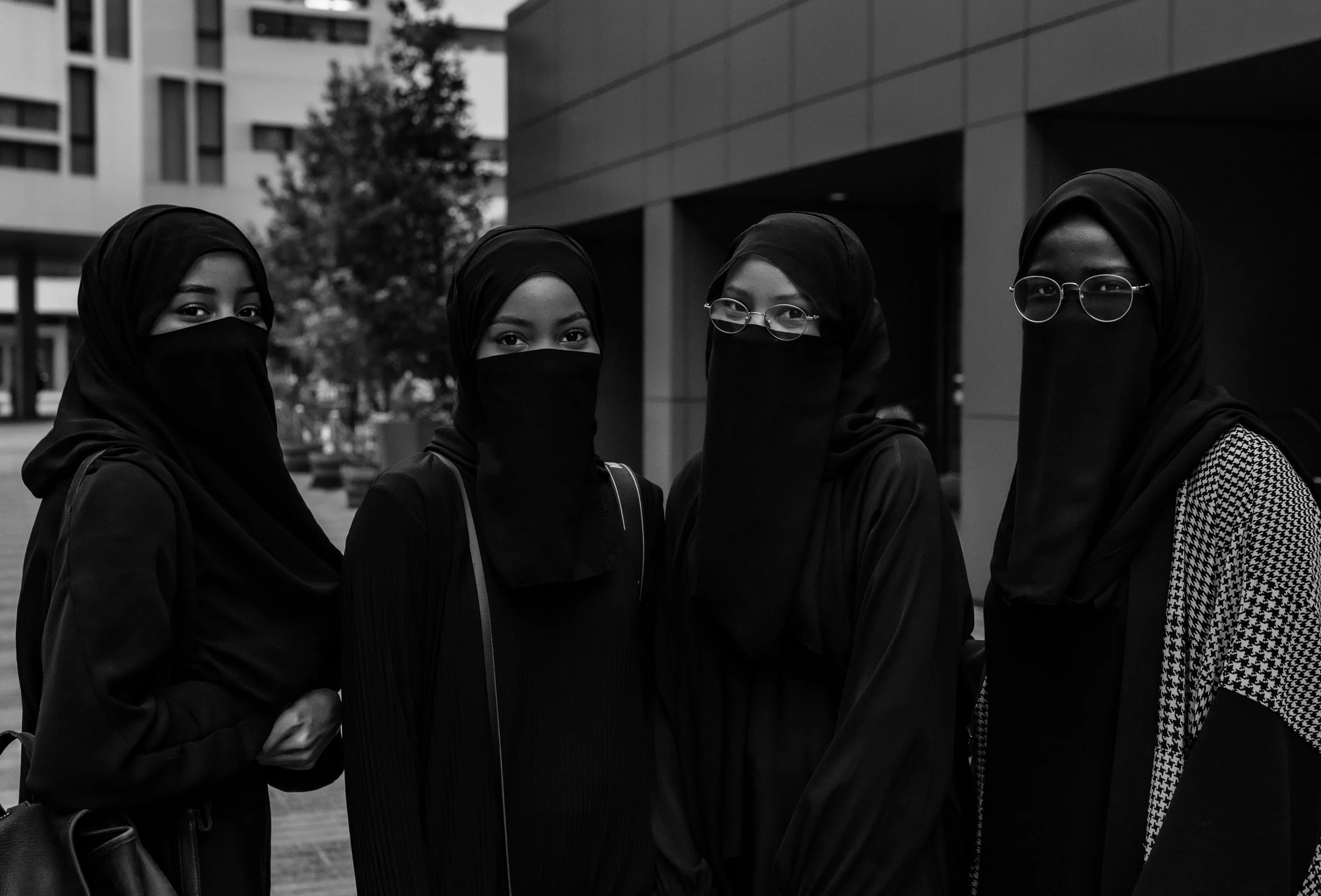 Four women wearing hijabs and face masks standing outdoors.