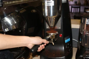 First step for the barista is to pack the coffee grounds from the coffee grinder into a metal portafilter.