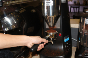 First step for the barista is to pack the coffee grounds from the coffee grinder into a metal portafilter.
