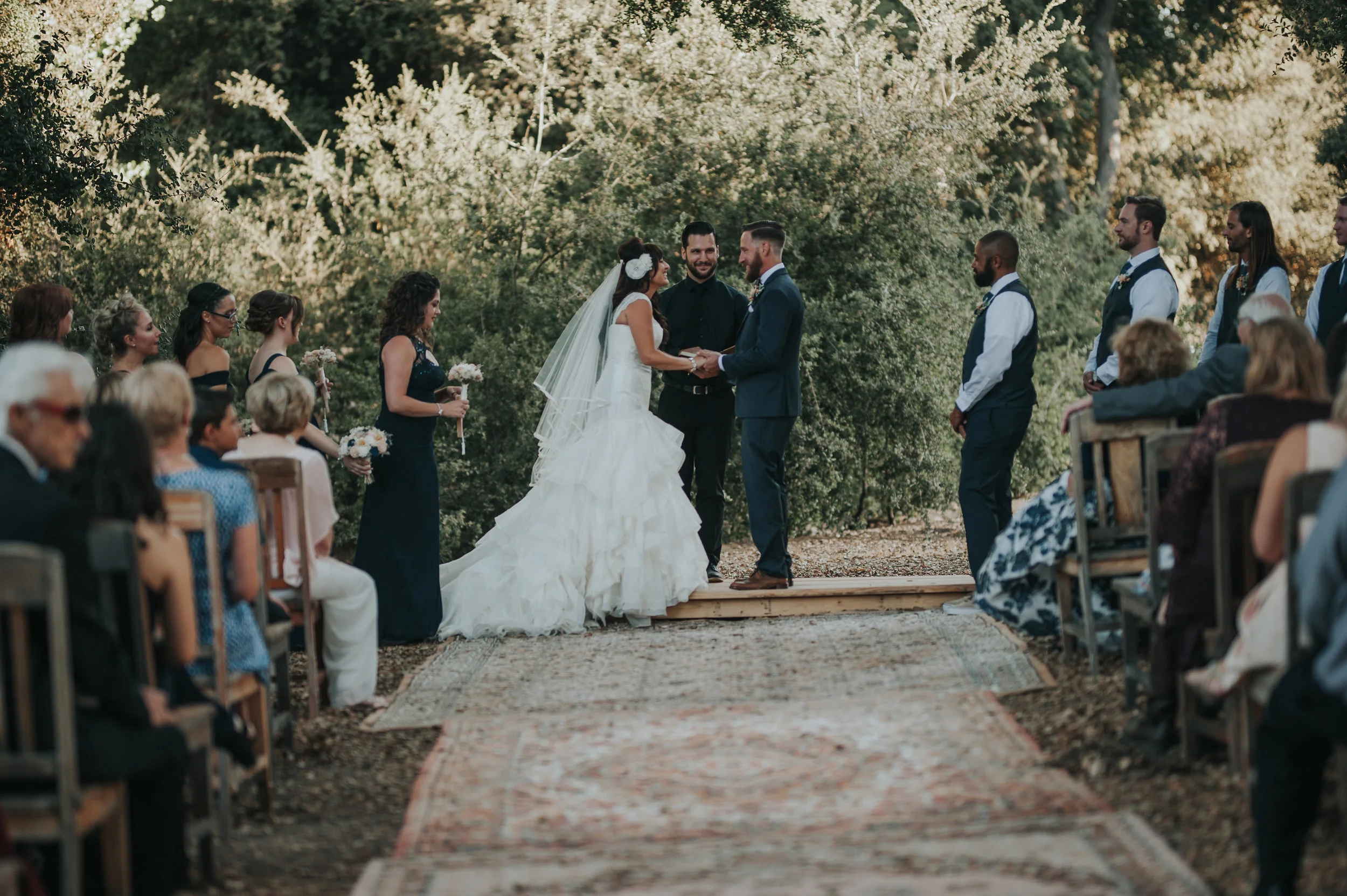 Bride wearing Zac Posen with her groom making her vows in a aisle of vintage rugs in the Temecula Valley.