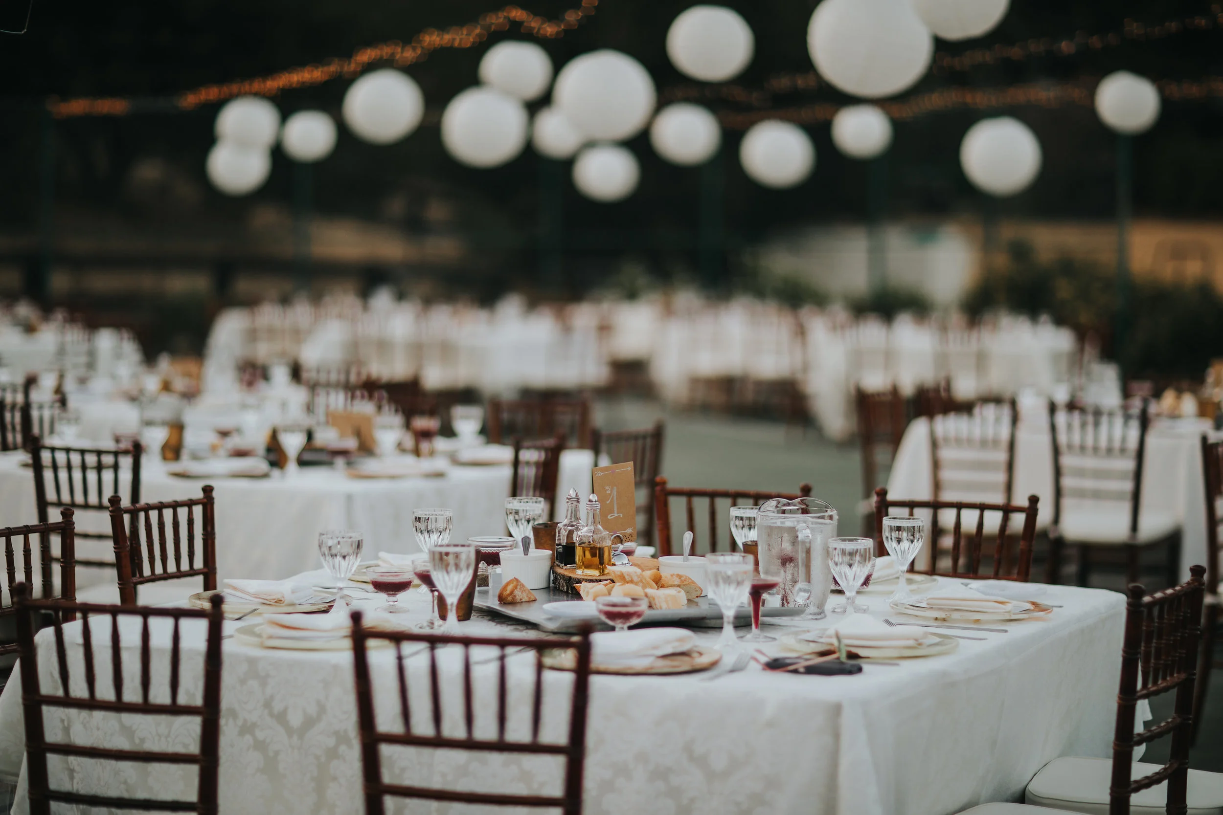 Square tables and Chiavari chairs at an outdoor wedding reception in the Temecula Valley. Chinese lanterns and twinkle lights overhead.