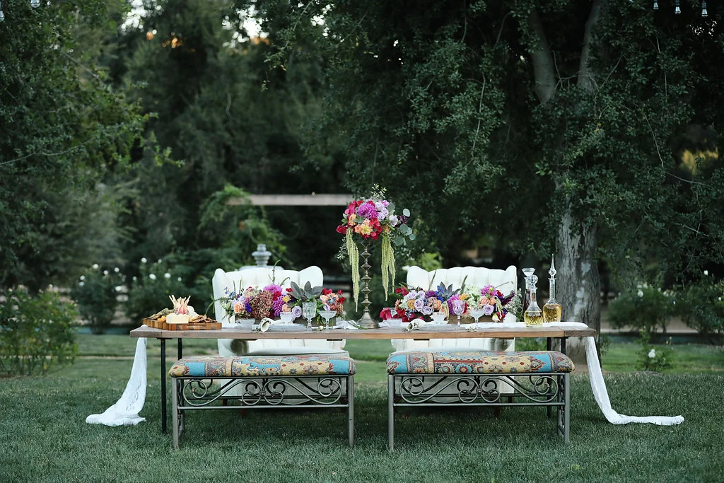 Bohemian wedding table with iron benches and tufted chairs. Vintage rentals.