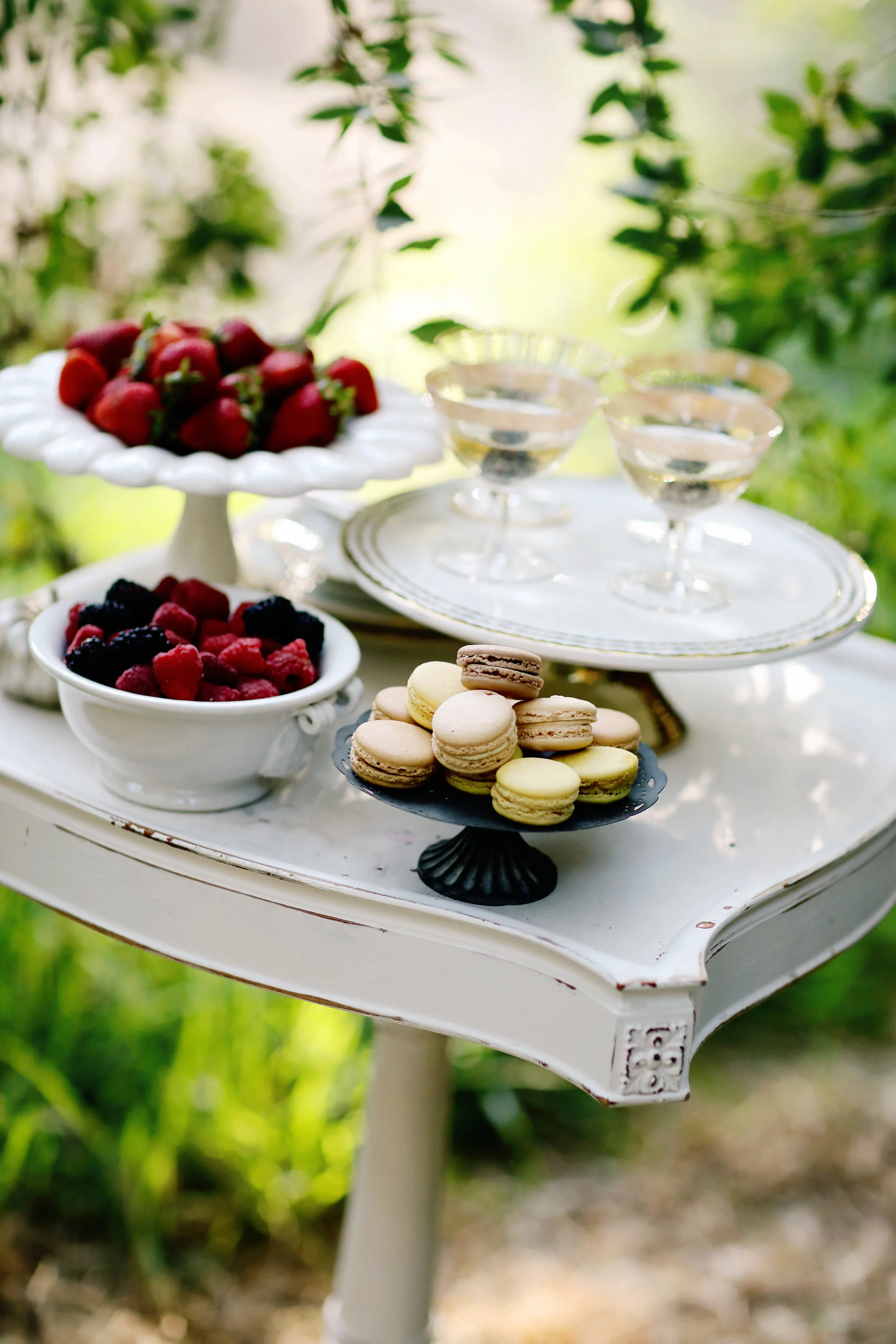 Vintage antique white wooden side table with desserts on the top for a wedding. Macaroons on milk glass pedestals.