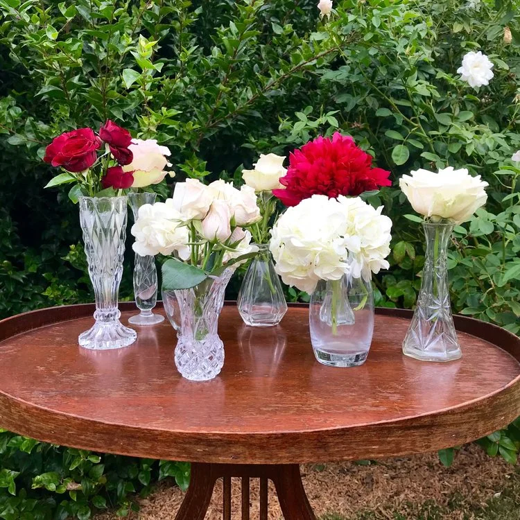 Assorted small cut glass vases with red and white flowers.