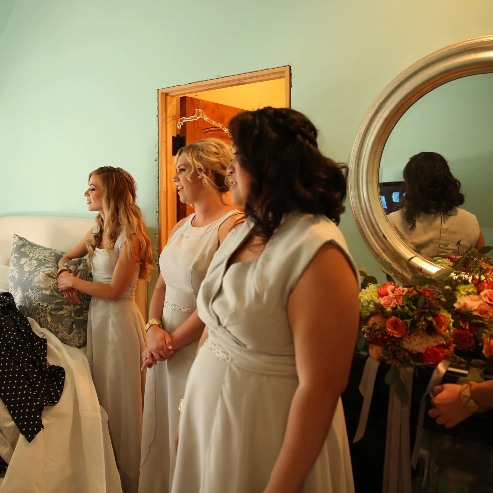 Bridesmaids gaze at the bride as she puts on her wedding dress while they all get ready for the wedding ceremony.