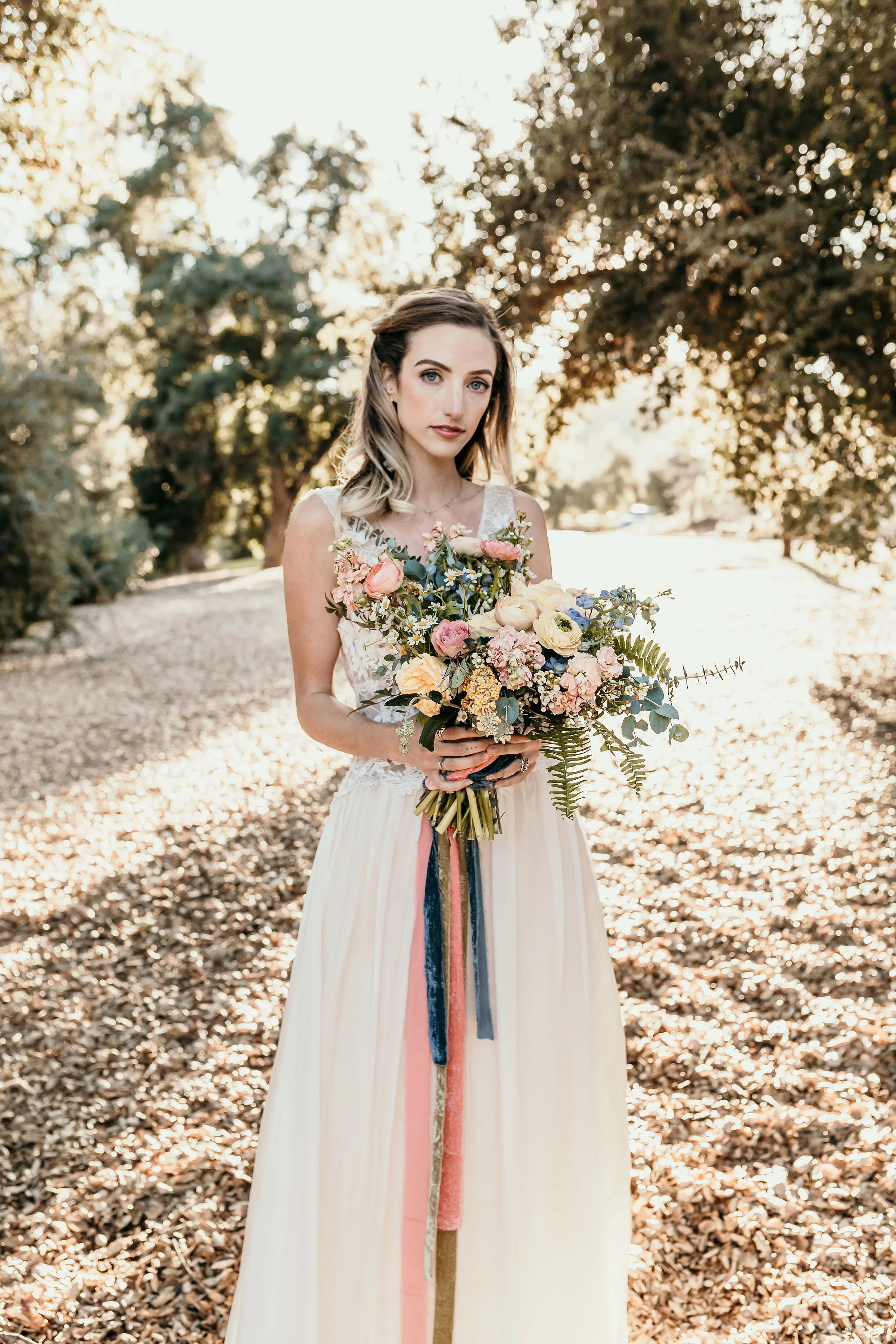 Alice in Wonderland bride holding her bridal bouquet which is done in pastel pinks with long silk ribbon.