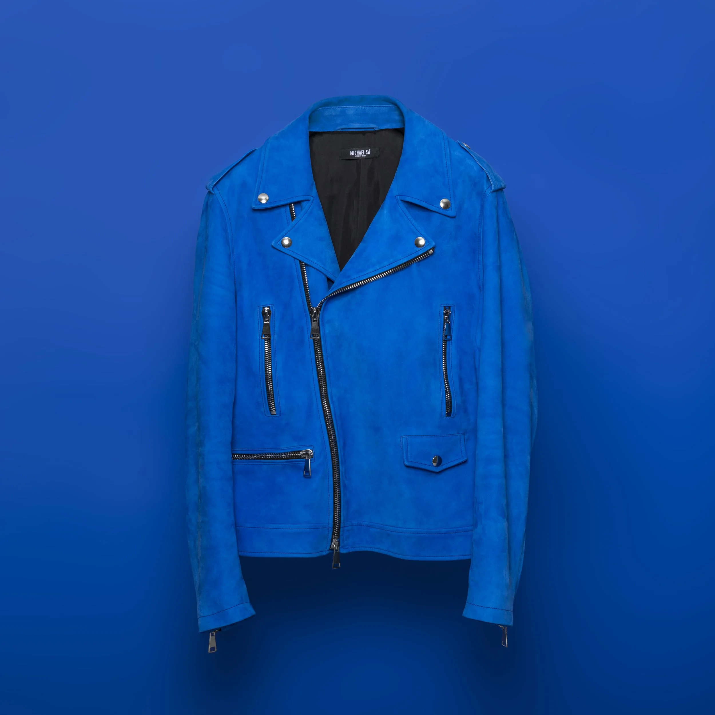 Blue leather biker jacket with zippers and metal studs on a blue background.