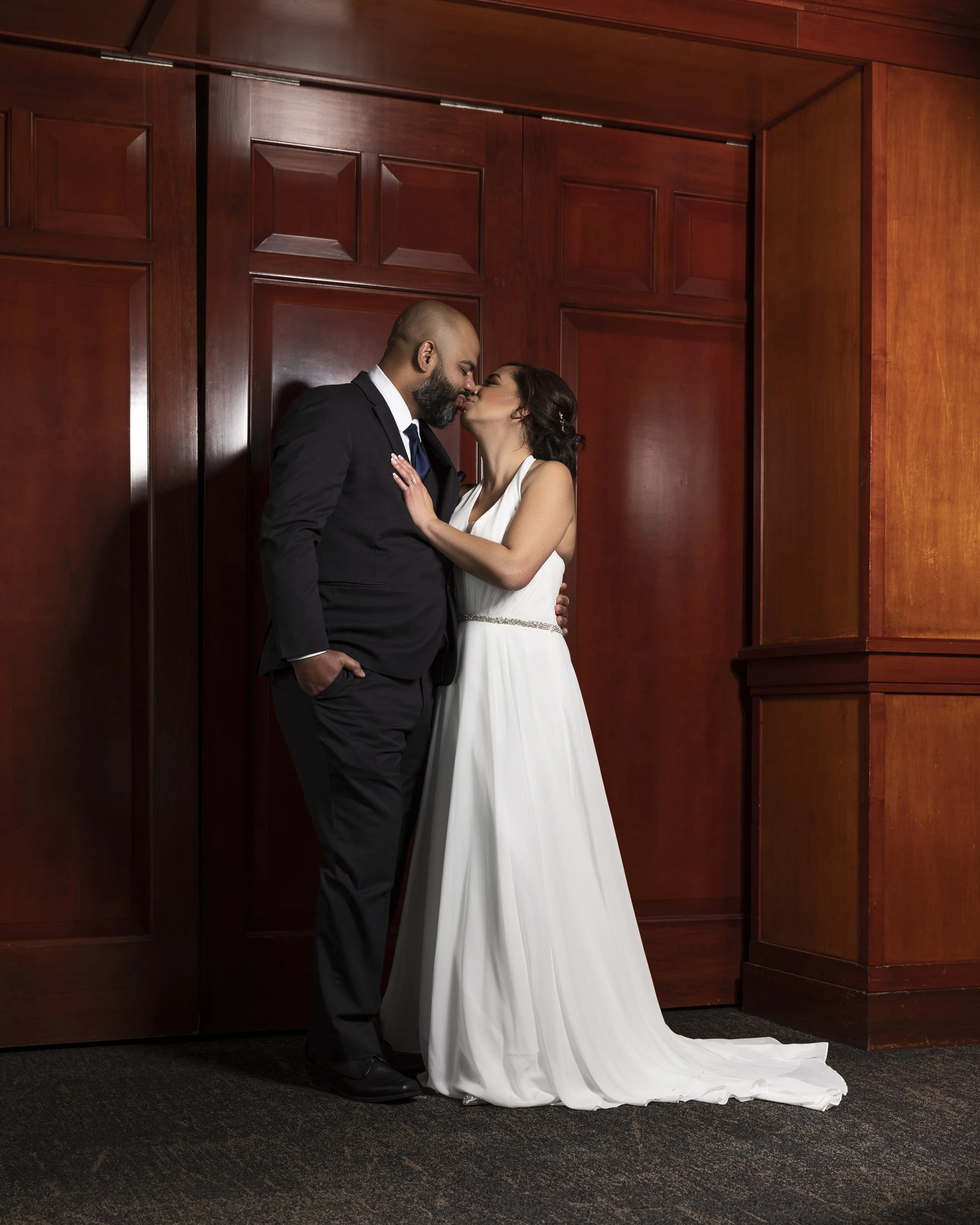Bride and groom standing close, embracing, and smiling in front of wooden double doors.