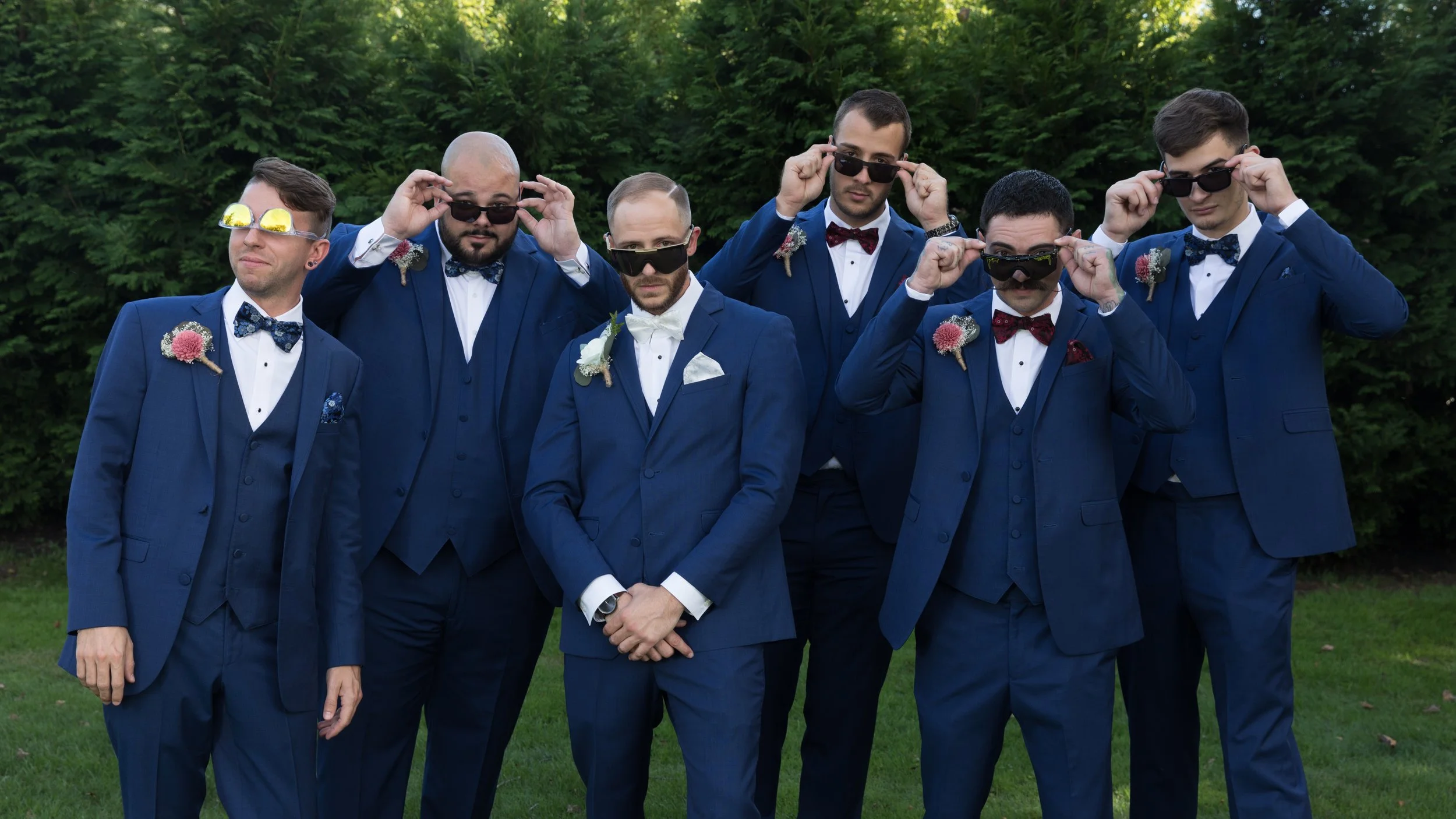 Groomsmen in blue suits wearing sunglasses, posing outdoors.