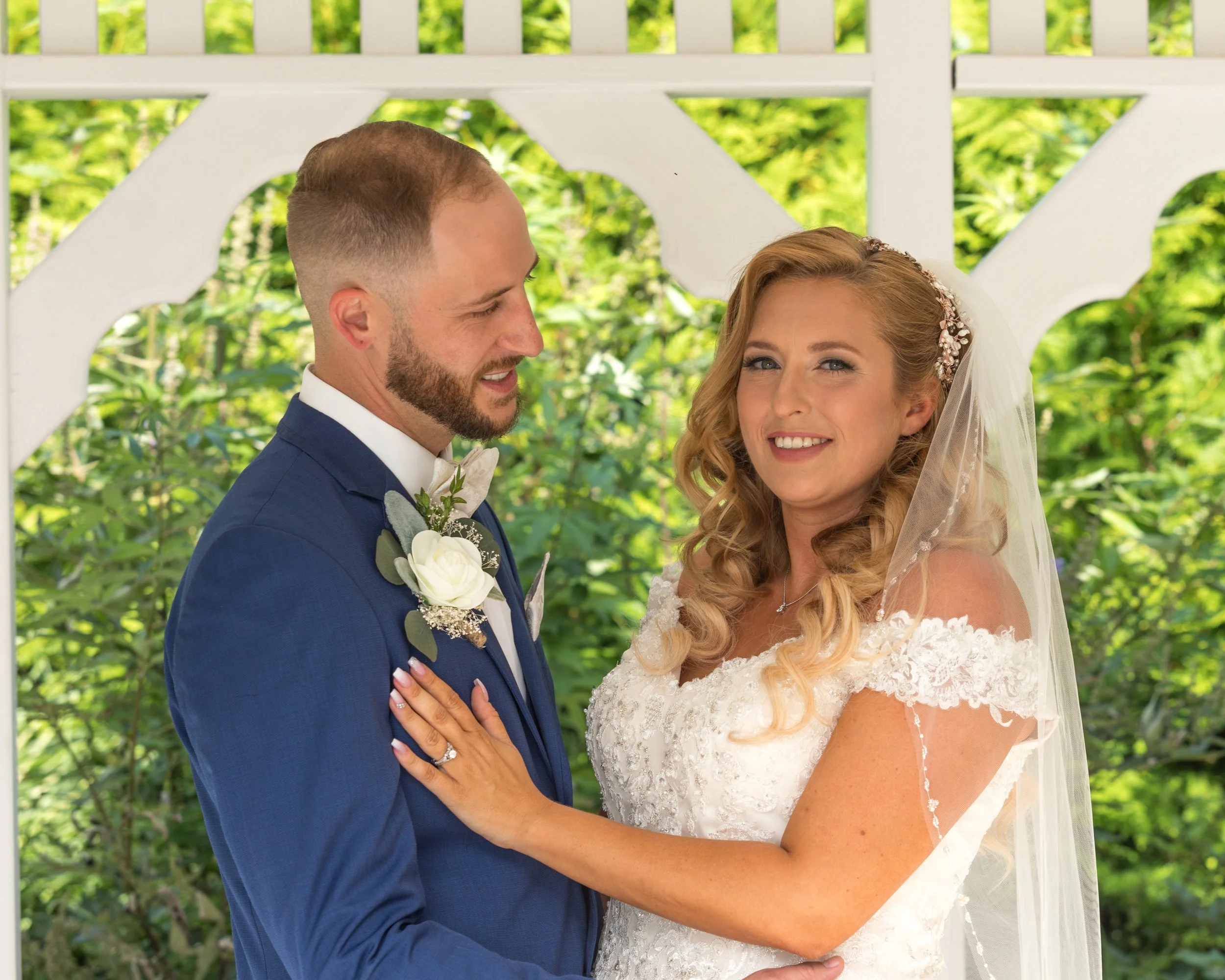 Bride and groom in wedding attire posing together under an outdoor gazebo.