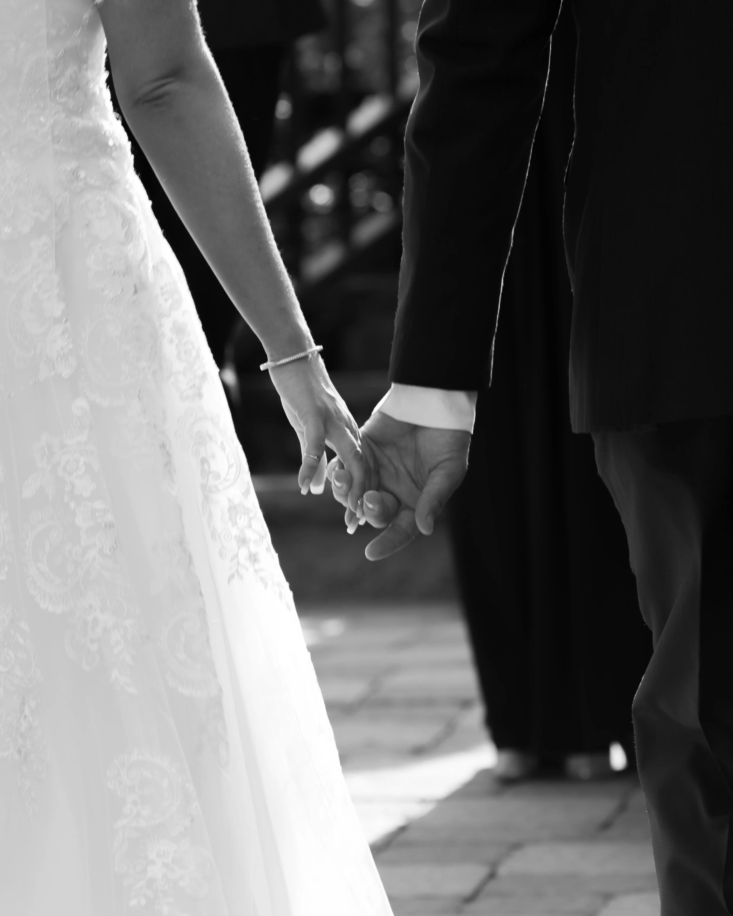 Bride and groom holding hands, black and white photo, wedding attire.