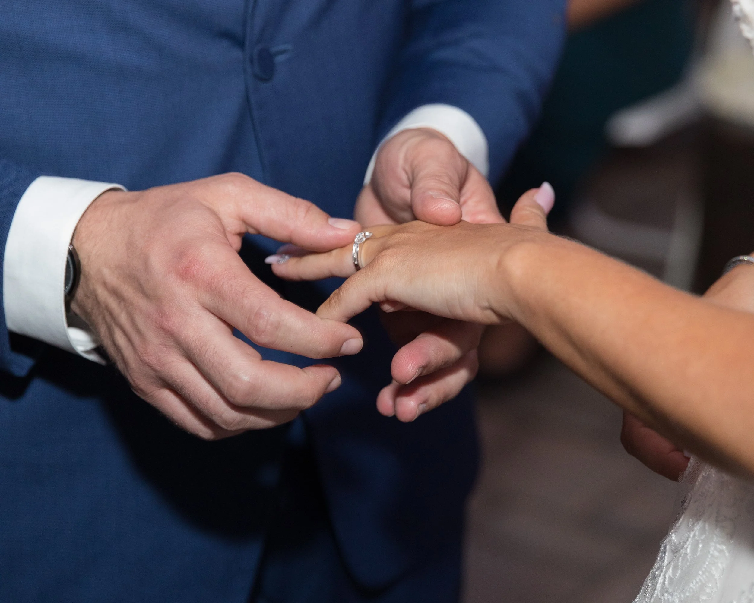 A suited man places a wedding ring on a woman's finger during a ceremony, symbolizing marriage and commitment.