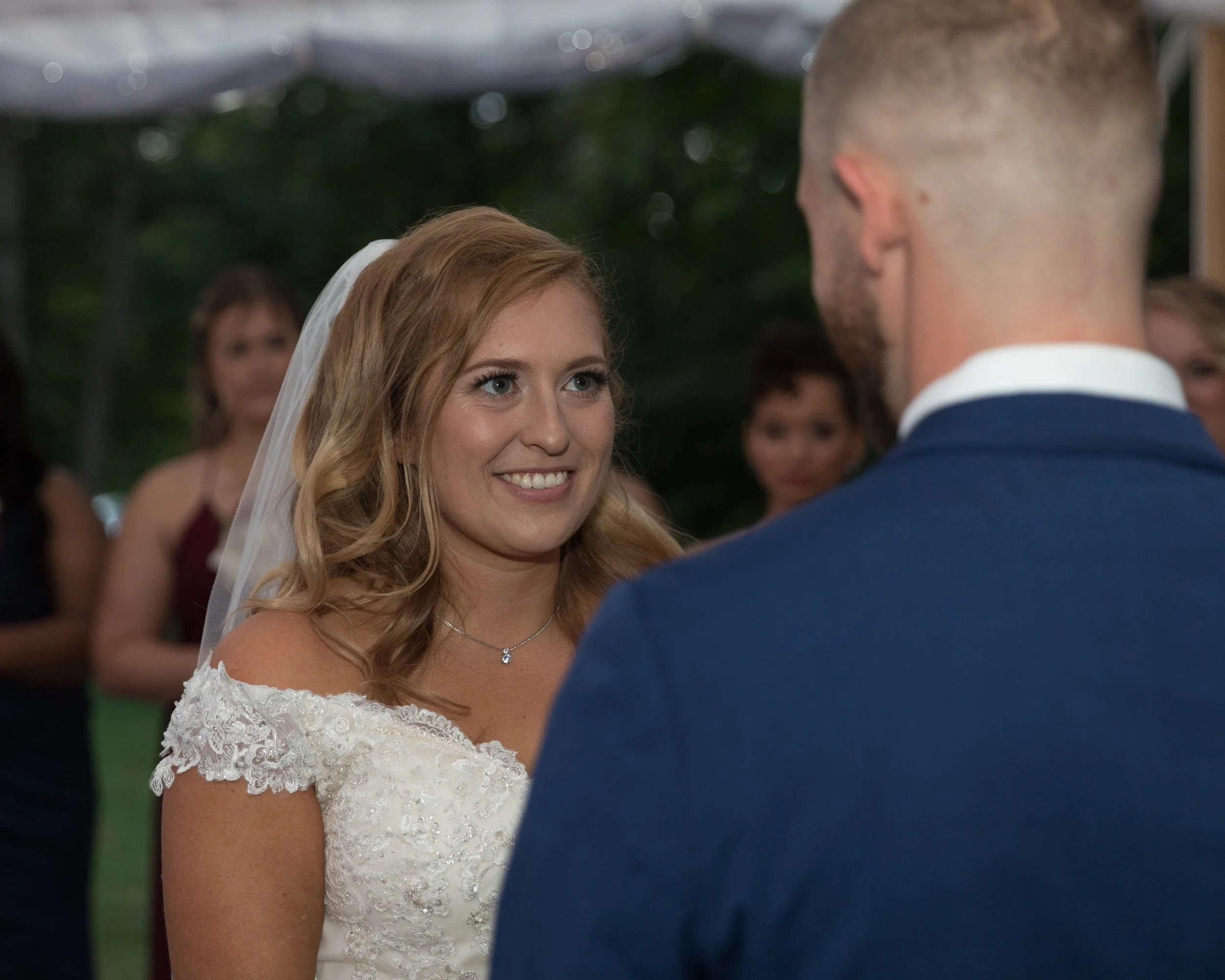 Bride and groom during wedding ceremony, bride in white dress and veil, groom in blue suit, outdoors.