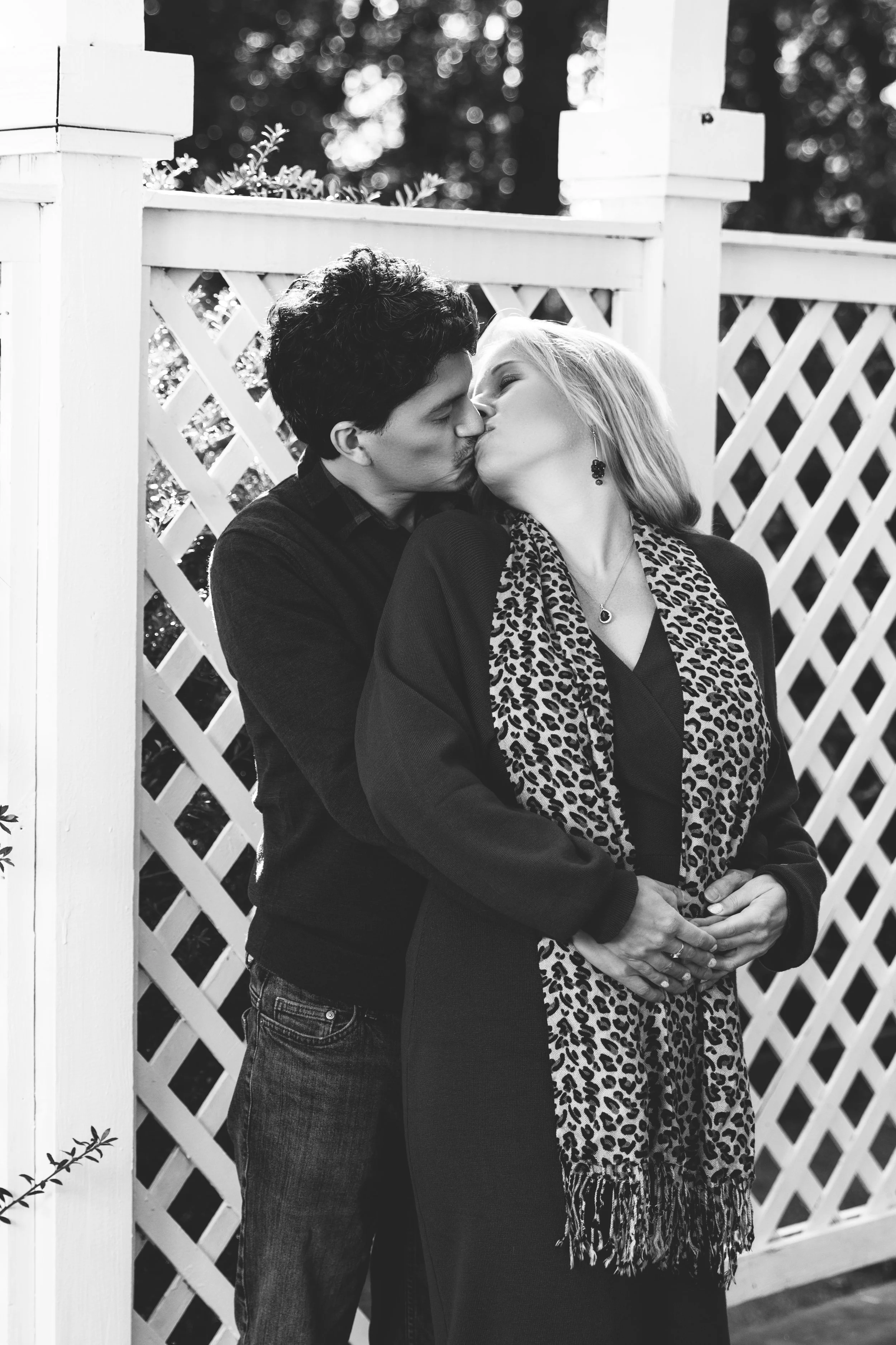 Black and white photo of a couple kissing in front of a lattice fence.