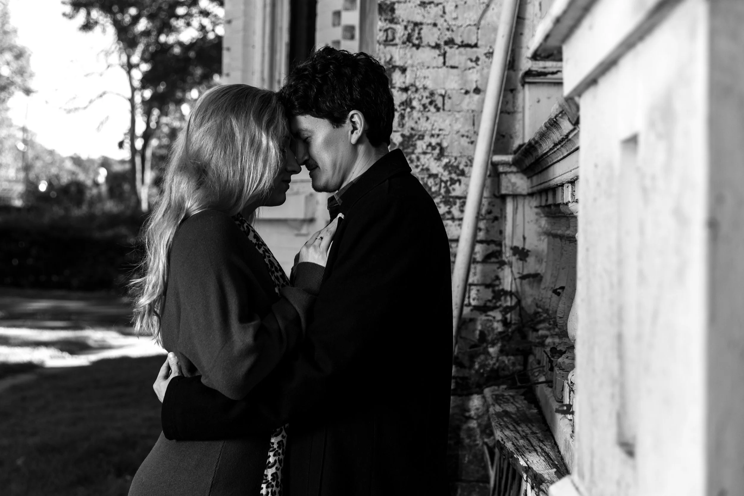 Black and white photo of a couple embracing closely in front of a brick wall.