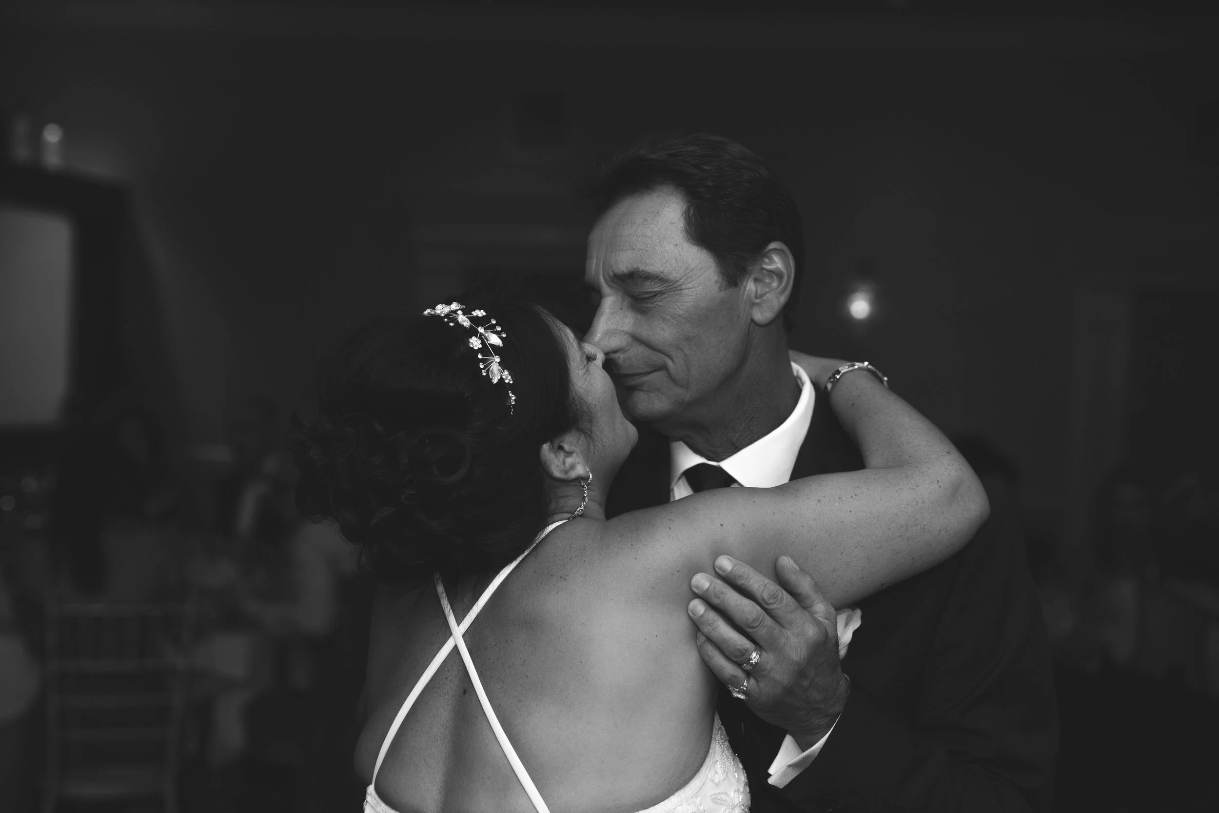 Black and white photo of a woman in a white dress and a man in a suit dancing closely at an event.