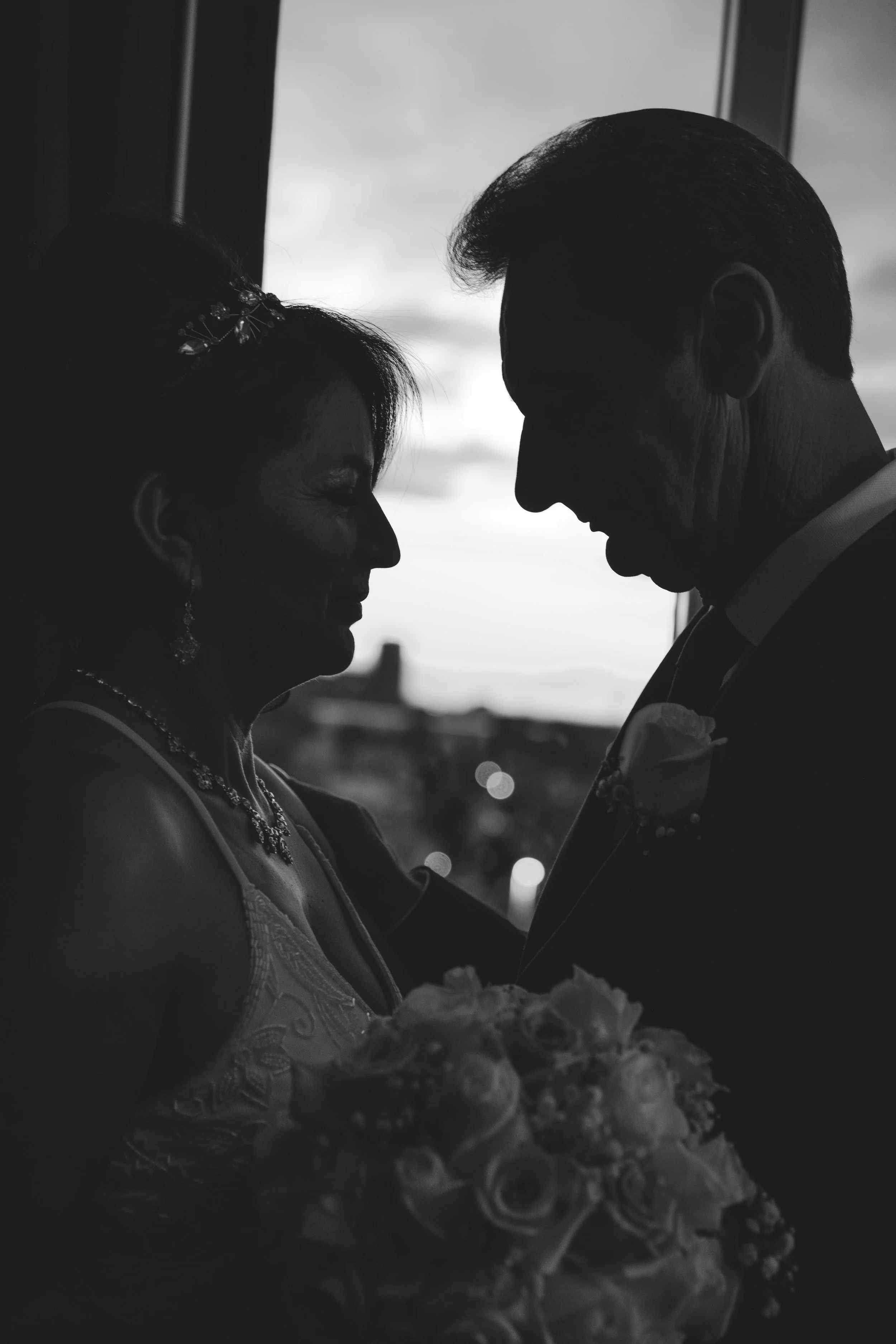 Silhouette of a bride and groom facing each other with a bouquet of flowers.