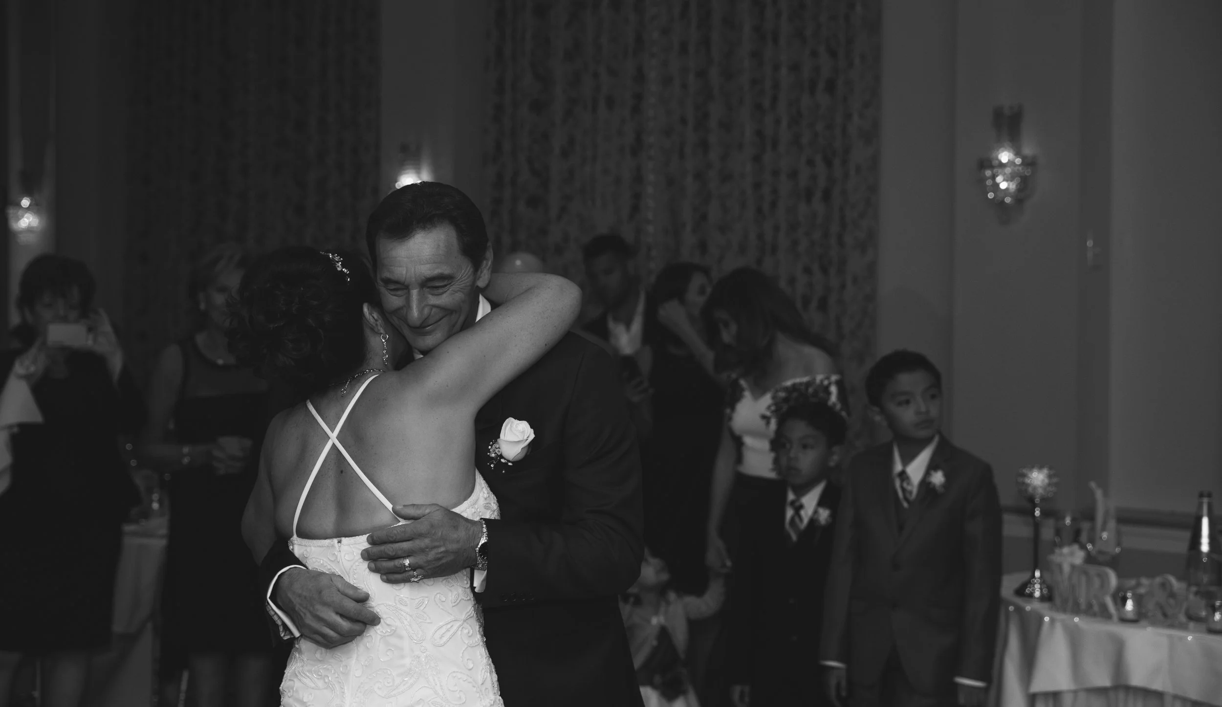 Bride and groom dancing together at a wedding reception with guests observing in a formal setting.