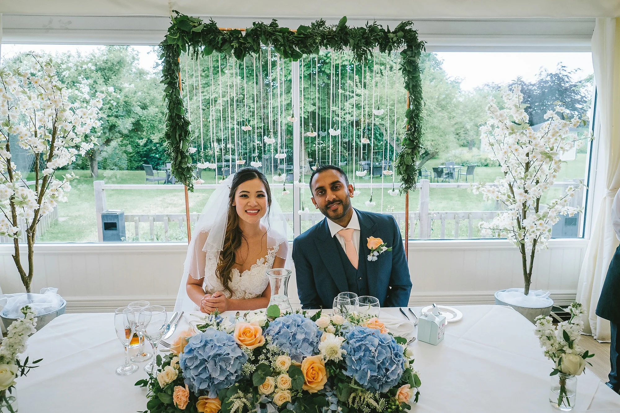 Sweetheart table at Essex garden wedding with peach and blue floral arrangement and hanging carnations on copper frame