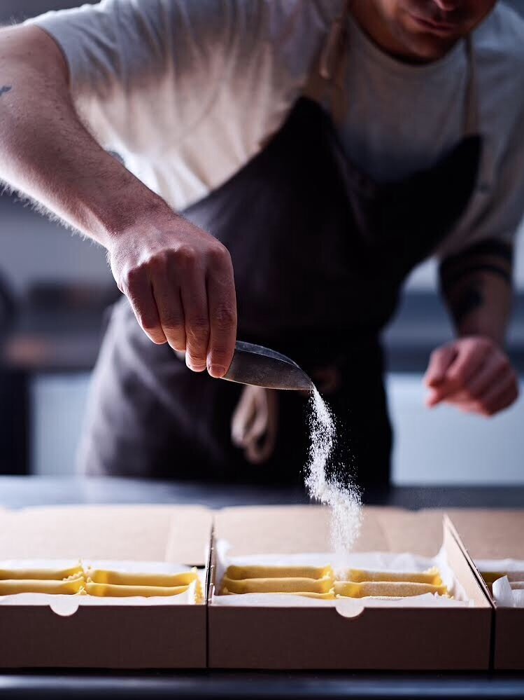 Person sprinkling flour over freshly made pasta in a box.