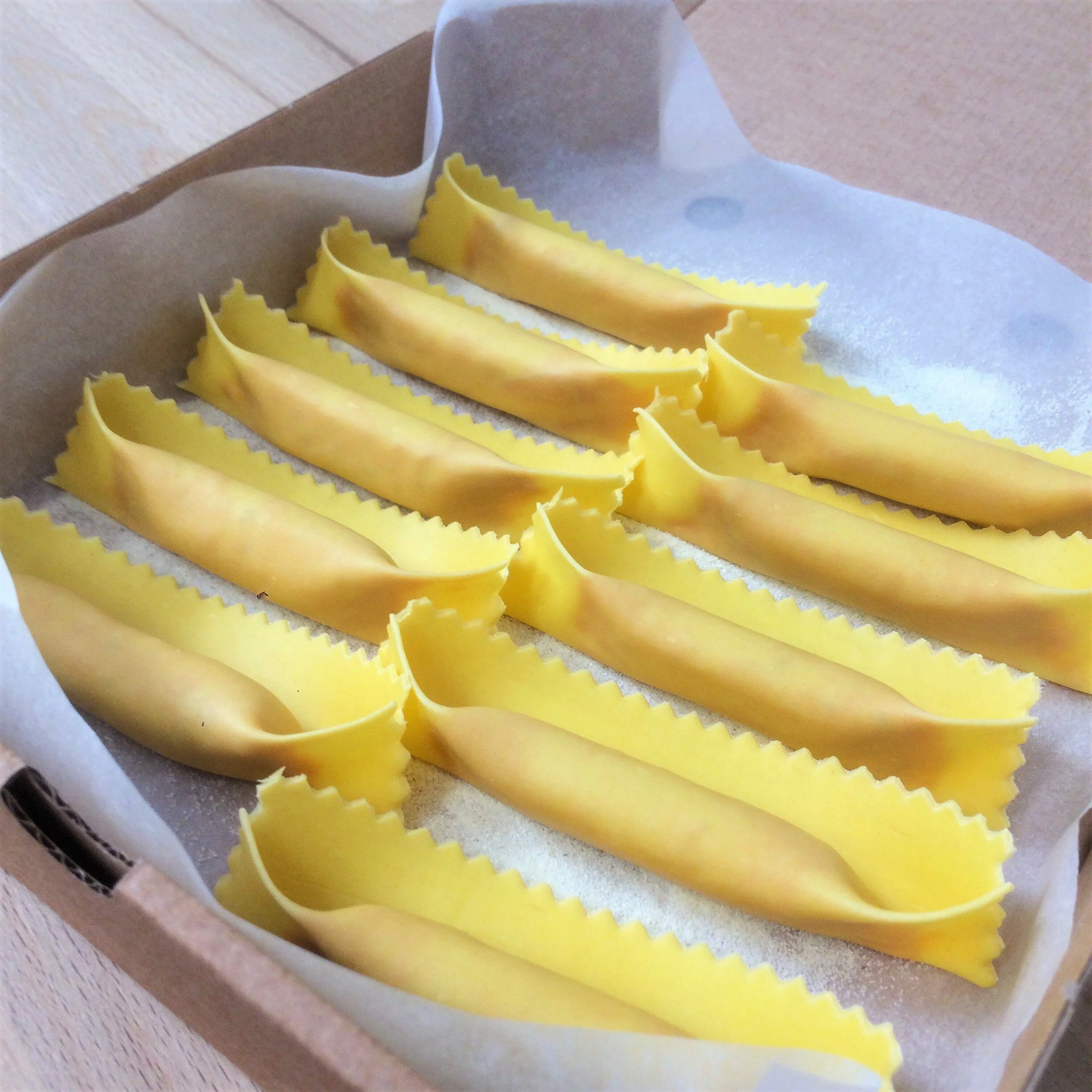 Uncooked yellow lasagna noodles on parchment paper in a cardboard box.