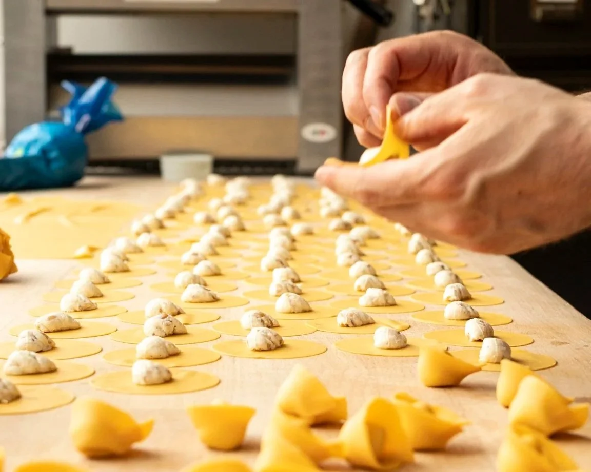 A person making pasta, placing dollops of filling on rolled-out pasta sheets.