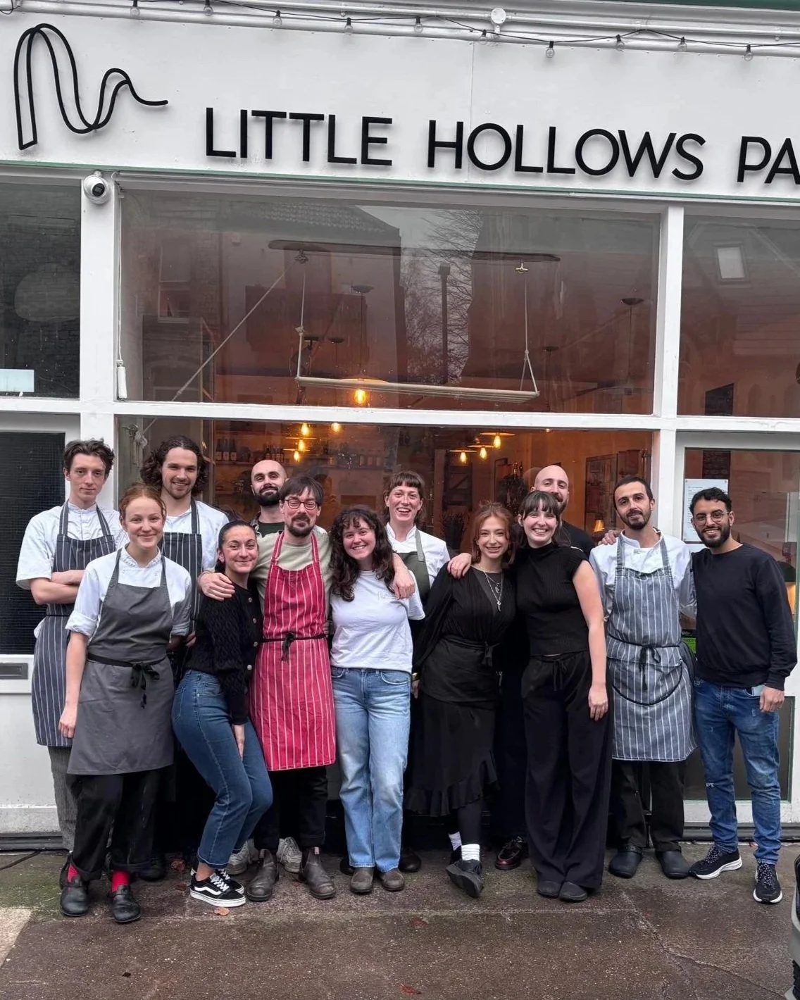Group of 12 people, including chefs and staff, standing outside the Little Hollows pastry shop, smiling and posing for a photo.