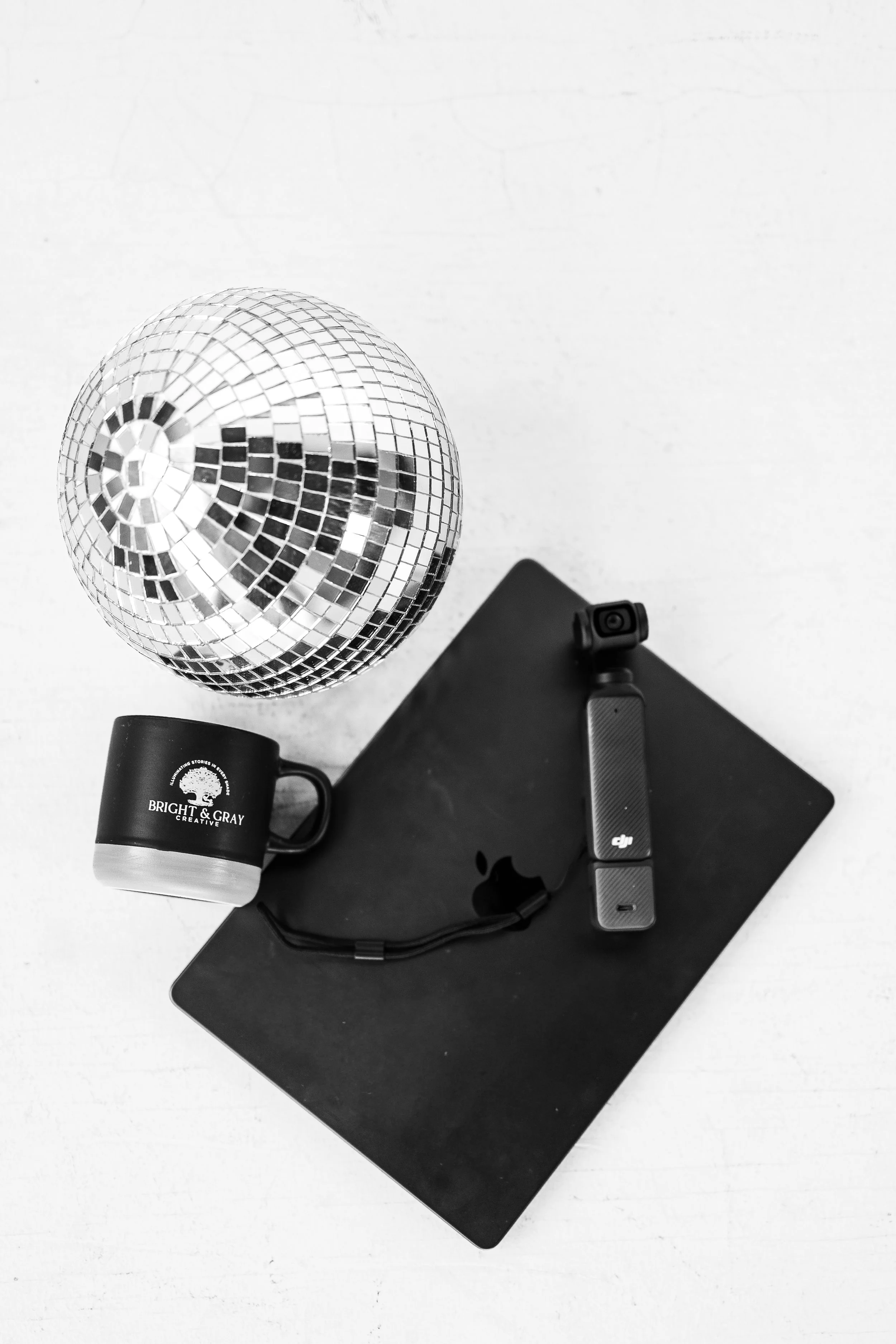 Bright & Gray Creative branded flat lay featuring a BGC coffee mug, DJI pocket camera, and disco ball in black and white, representing content creation and video production services for small businesses across the Southeast.