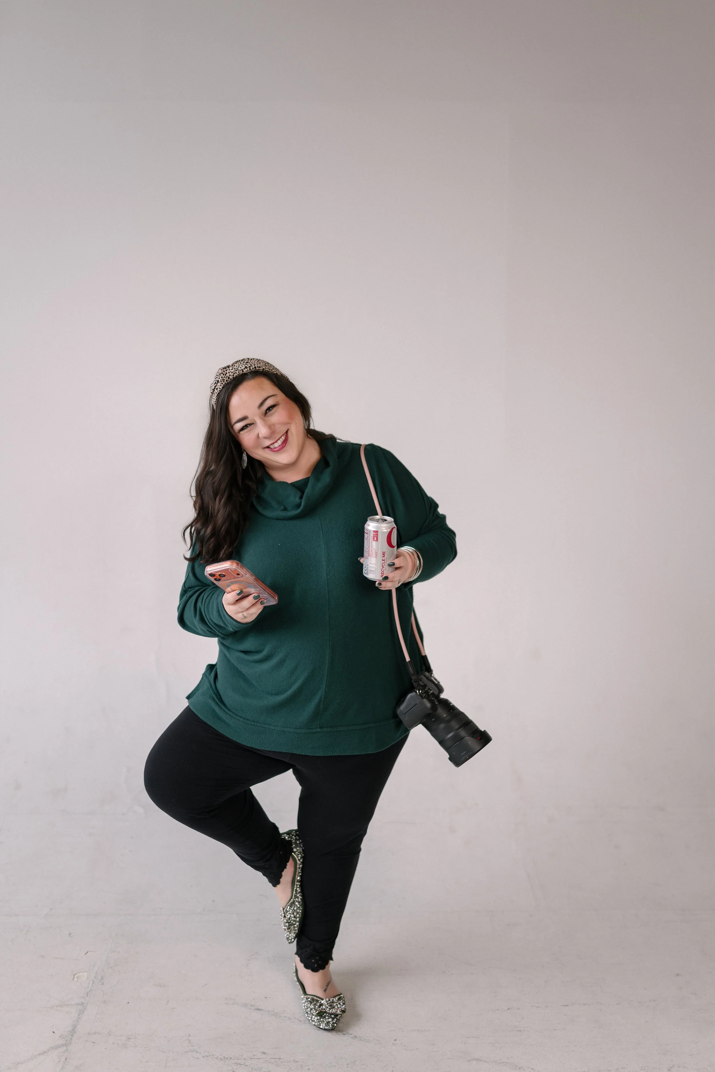 Portrait of Jessica Morales, founder and Creative Director of Bright & Gray Creative in Birmingham, AL, posing playfully in a studio portrait holding a camera, a phone, and a Diet Coke, wearing a green top, representing Birmingham Alabama branding