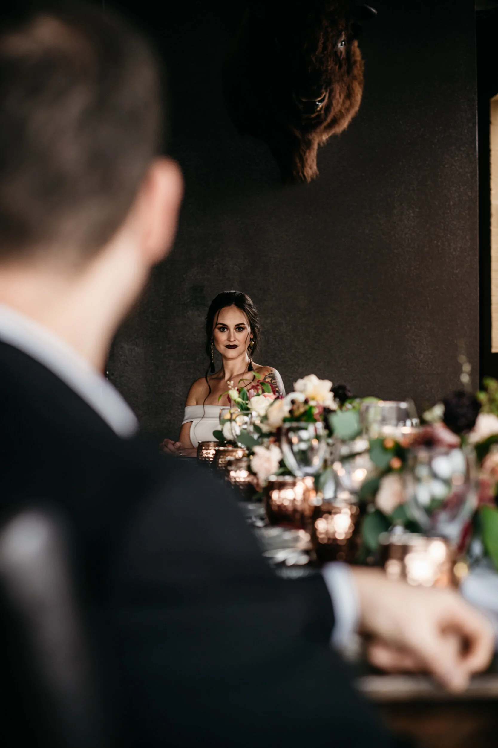 Bride sitting at edge of long table for moody, romantic distillery wedding designed by wedding planner Unions With Celia at Missouri Spirits. Photographed by Sean Reid.