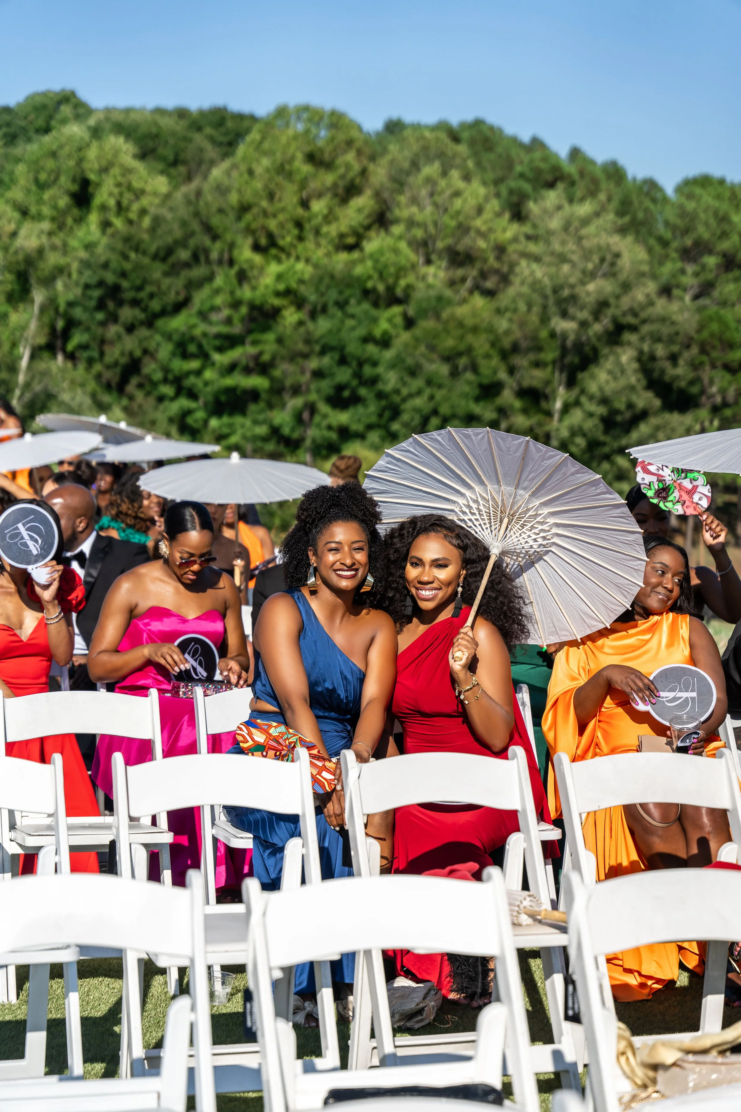 Group of women dressed in colorful dresses sitting outdoors during a wedding ceremony on a sunny day in Atlanta Ga. 