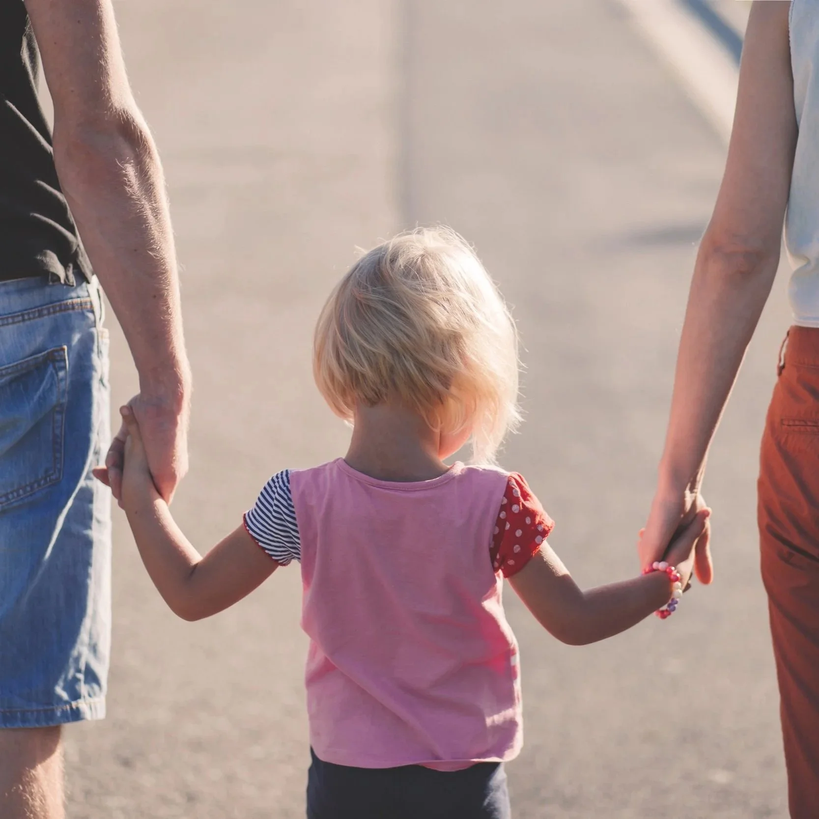 Photo d'un enfant tenant les mains de ses parents.