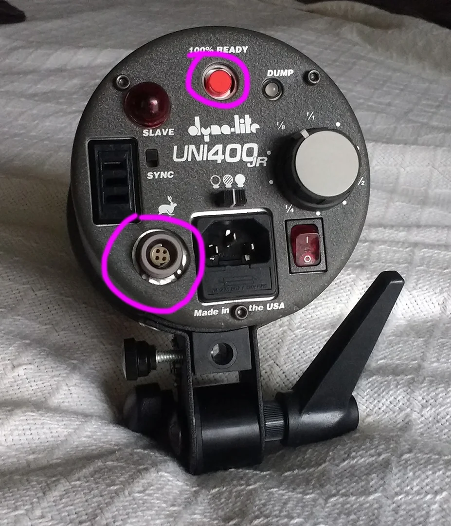 The light head, mended. The red button is the "dump" button (to release built up power when powering the flash head down a stop or more) and the grey/purple plug is for the Jackrabbit/battery. He used a c-clip on the Jackrabbit plug to secure it to the metal plate.