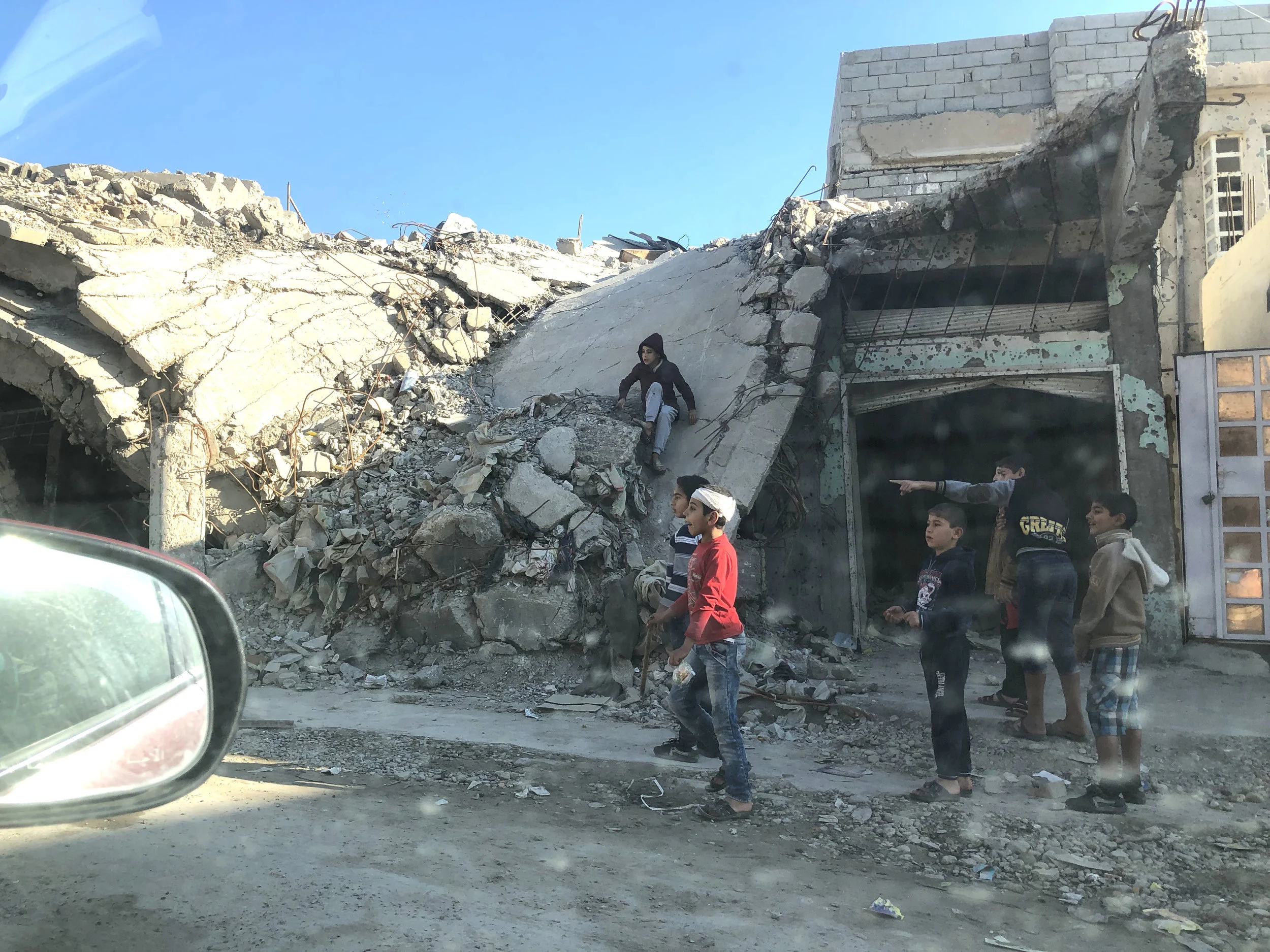 Children playing on rubble in western Mosul, as seen from the passenger seat of my translator’s car. November, 2018. (Rebecca Gibian)