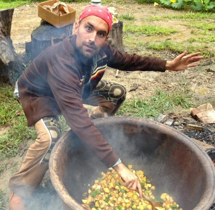 Joel Karabo Elliot cooks a stew with locally grown vegetables in a cast iron cauldron over an open fire in between bouts of rain from Hurricane Harvey. (photo by Nicole Garneau)