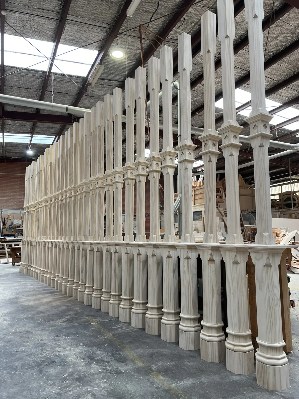 A long row of shaped and fluted timber posts standing in the workshop