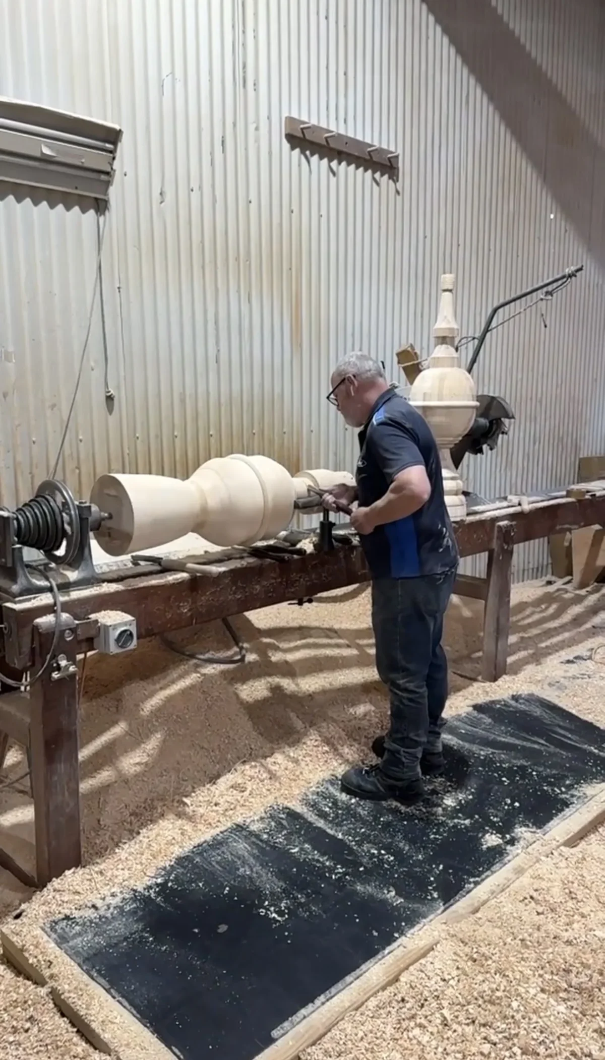 Craftsperson shaping a large timber component on a workshop lathe