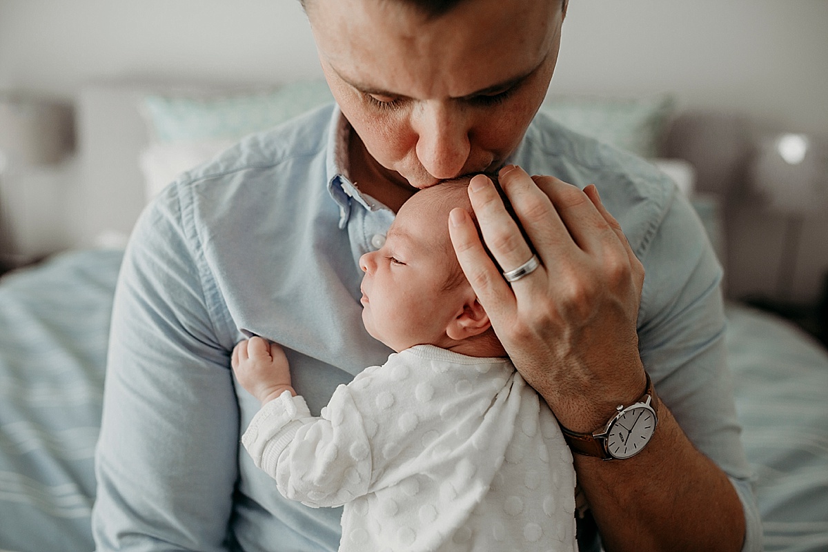 baby laying on dads chest, his hand cradling her head, kissing the top of her head