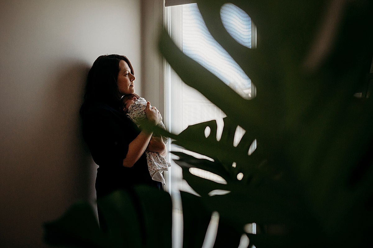 mum meaning against wall with new baby on her chest in beautiful light