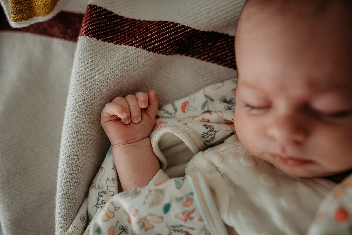 baby asleep on bed with hand up near head, fist clenched shut