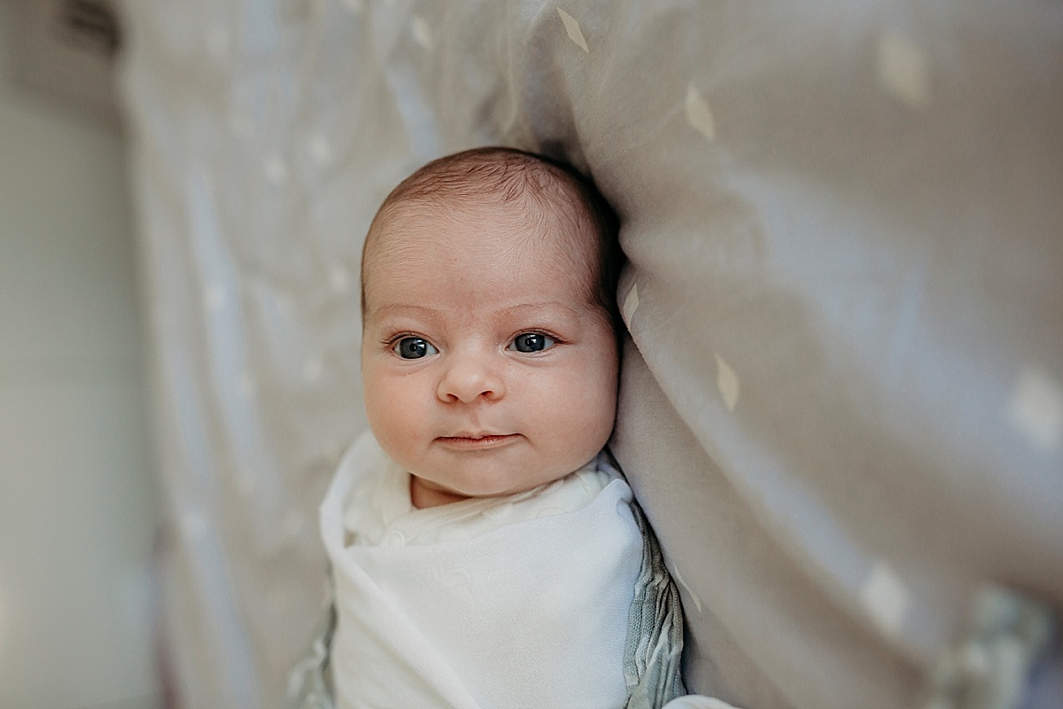 awake newborn smiling, wrapped up on bed
