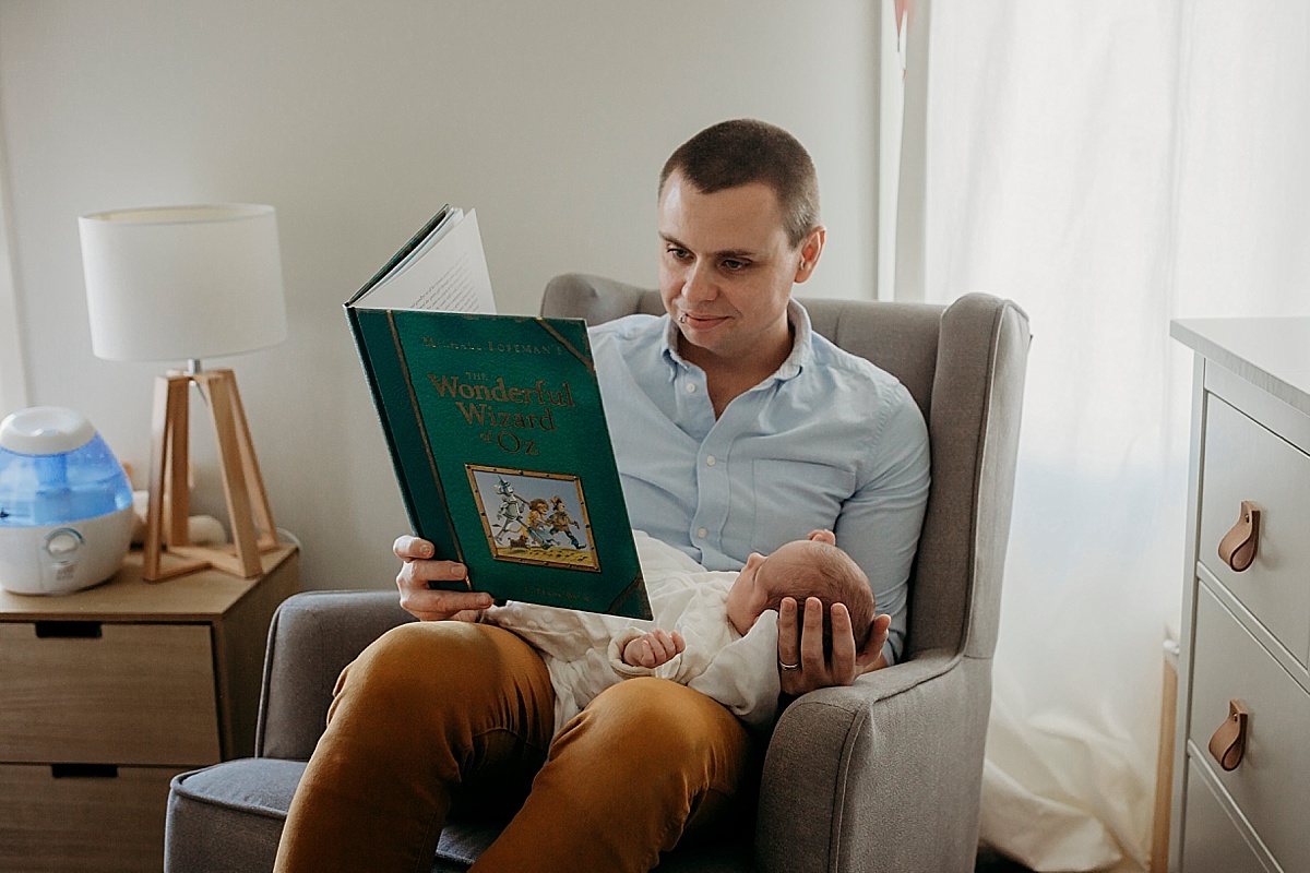Father reading to his newborn born baby girl in chair