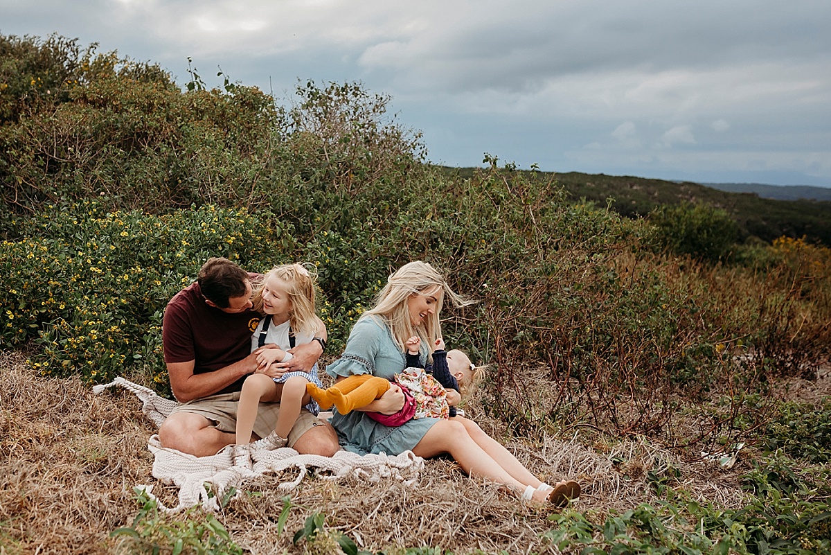 Mum dad and two daughters playing while sitting down on picnic rug