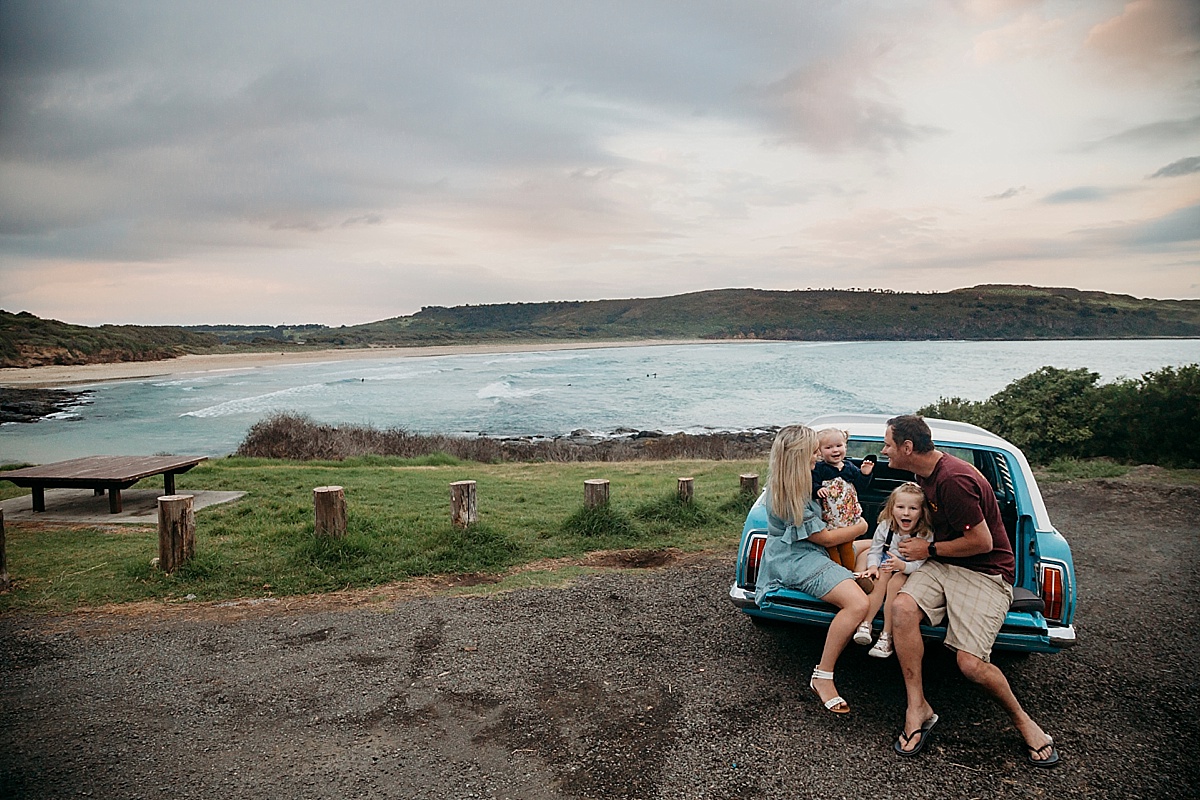 Family sitting on back of car, looking over the ocean
