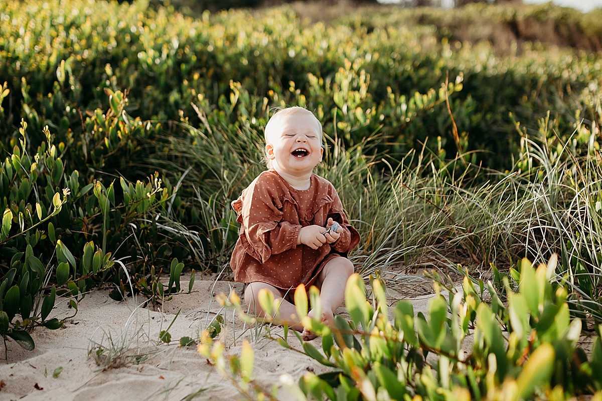 Little girl sitting on beach laughing