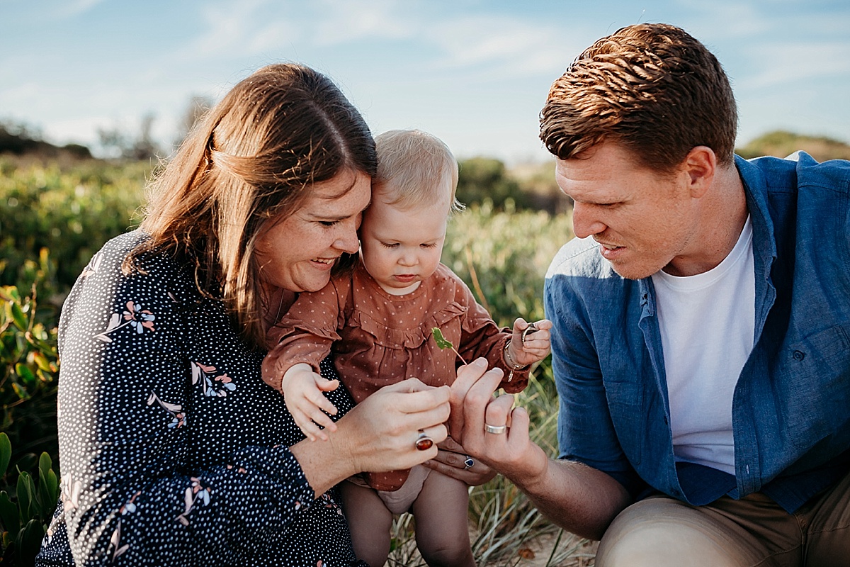 Mum holding baby girl sitting next to dad looking at flower