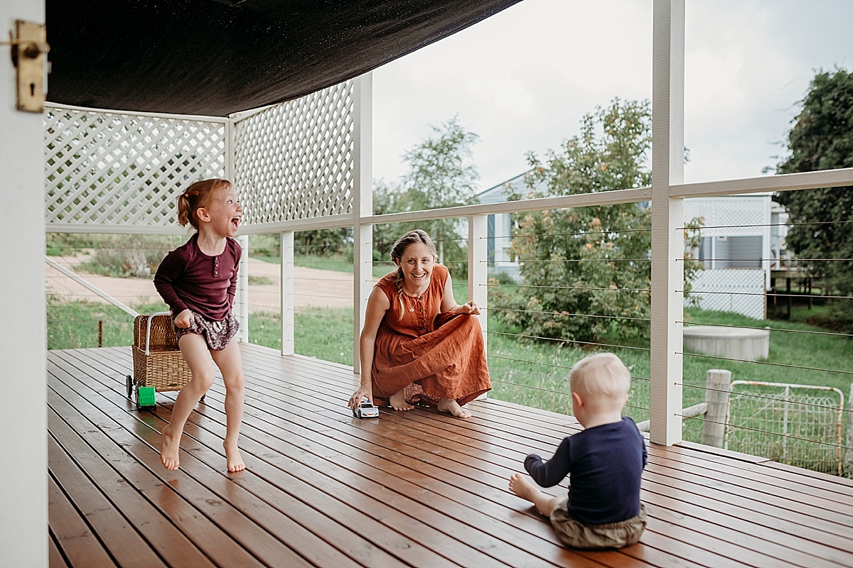 little girl dancing while mum and son play on deck with cars