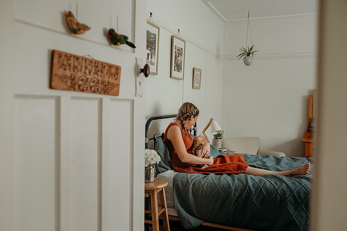 looking through bedroom door to mum and newborn sitting on bed